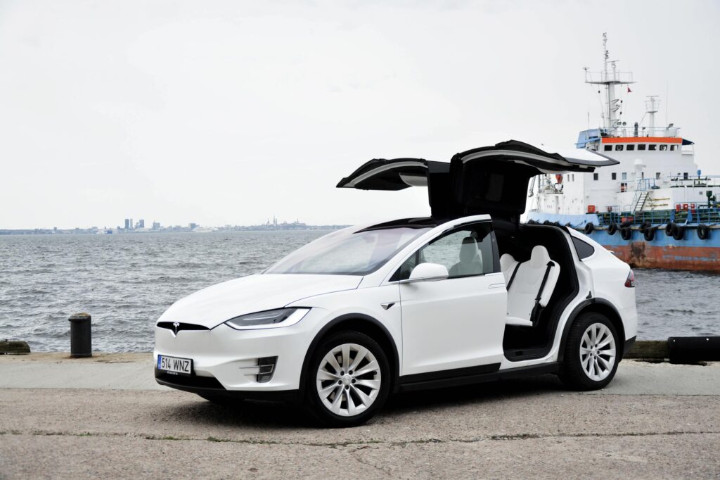 Valge Tesla Model X avatud tiibustega sadamas